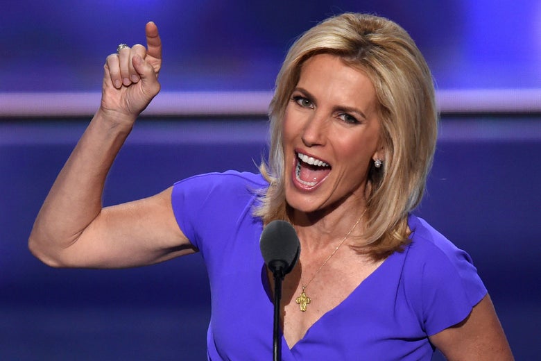 Ingraham smiles widely and points upward while standing behind a podium on a stage.